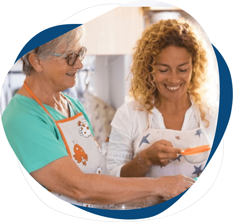 Two women are smiling while one of them is holding a carrot.