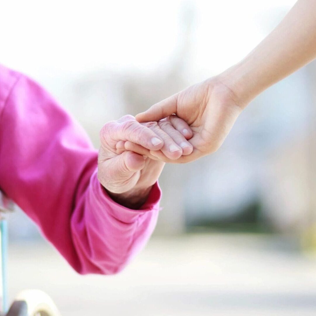 A person holding another persons hand while standing next to a fence.