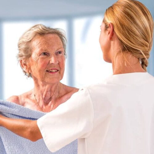 A woman in white shirt holding up a towel to an older person.